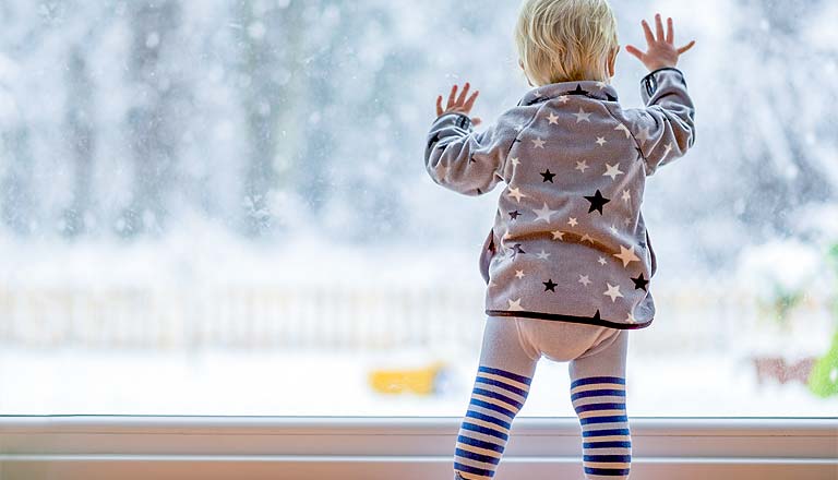 Kind schaut aus Fenster auf Winterlandschaft